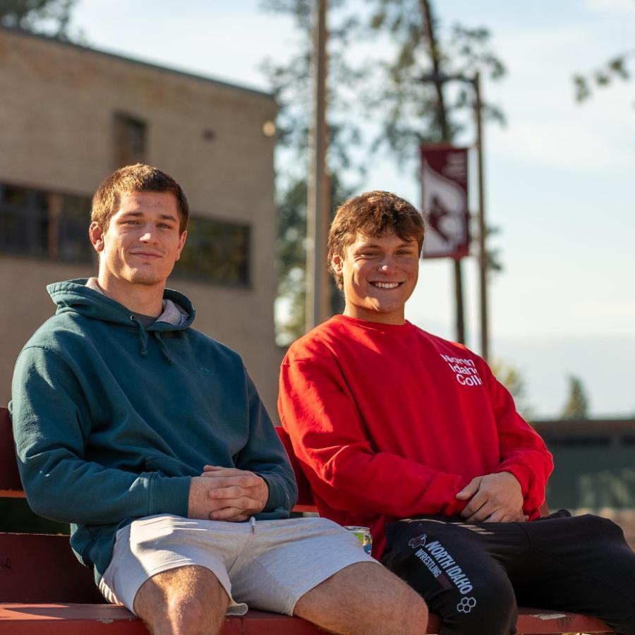 2 male students sitting on bench in the fall