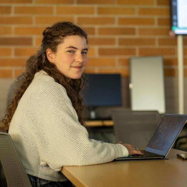 Female student at table smiling working on computer