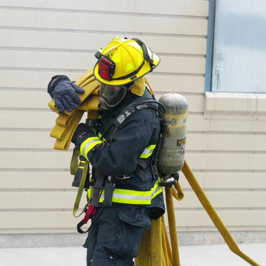 900x900 male fire fighter student donned in fire gear carrying a fire hose