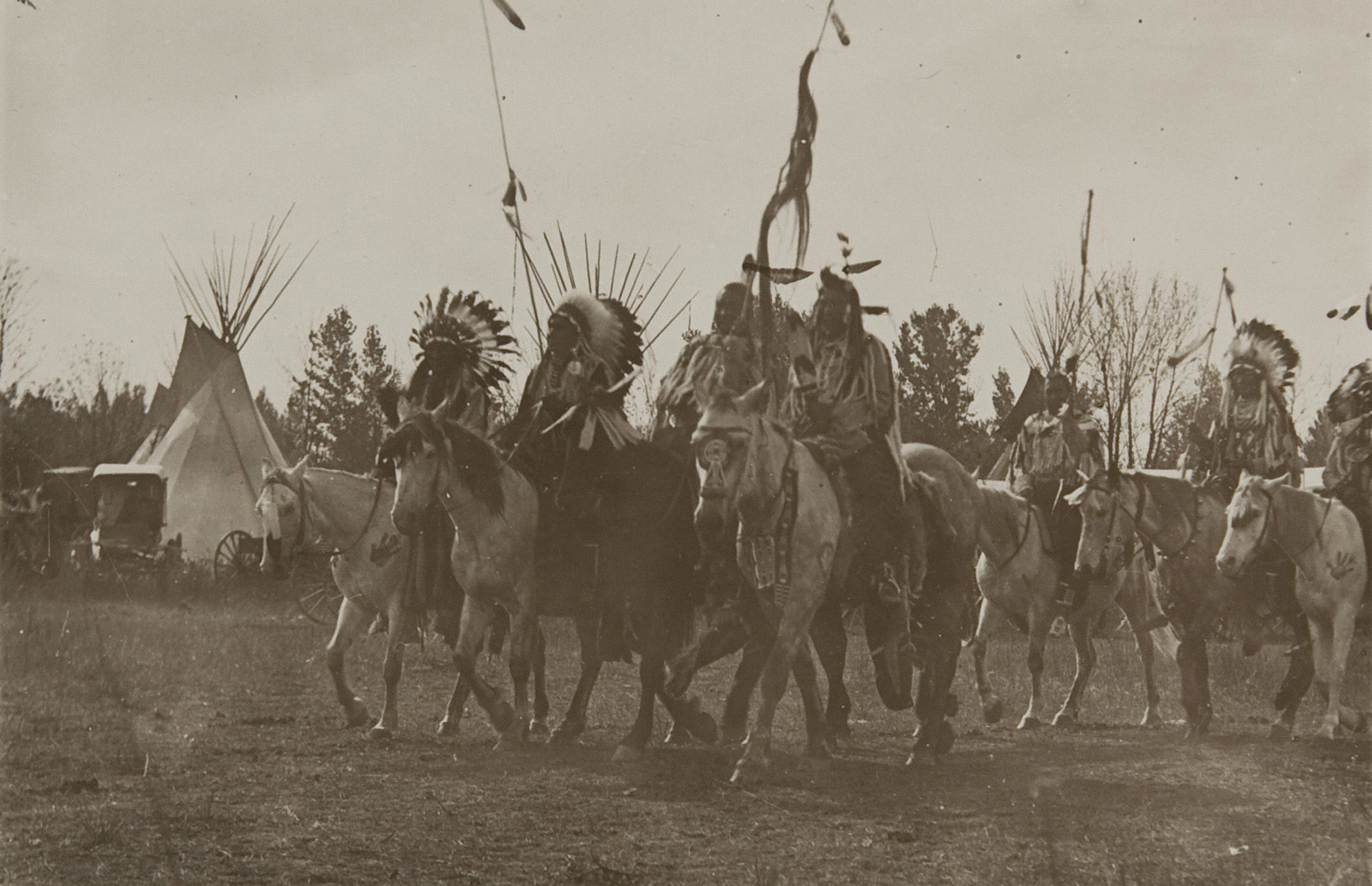 Native Americans wearing headdresses on horseback