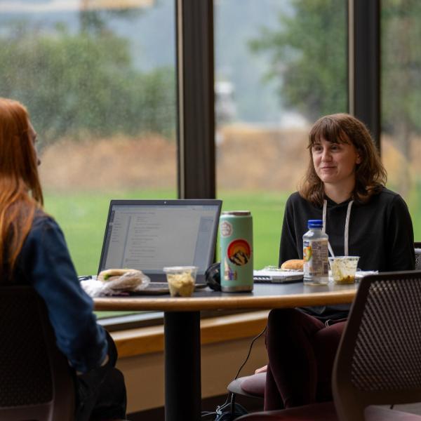 2 students at table at sub eating and working on computer