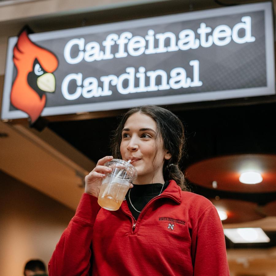 900x900 a female student drinking a cold drink in front of Caffeinated Cardinal Cafe