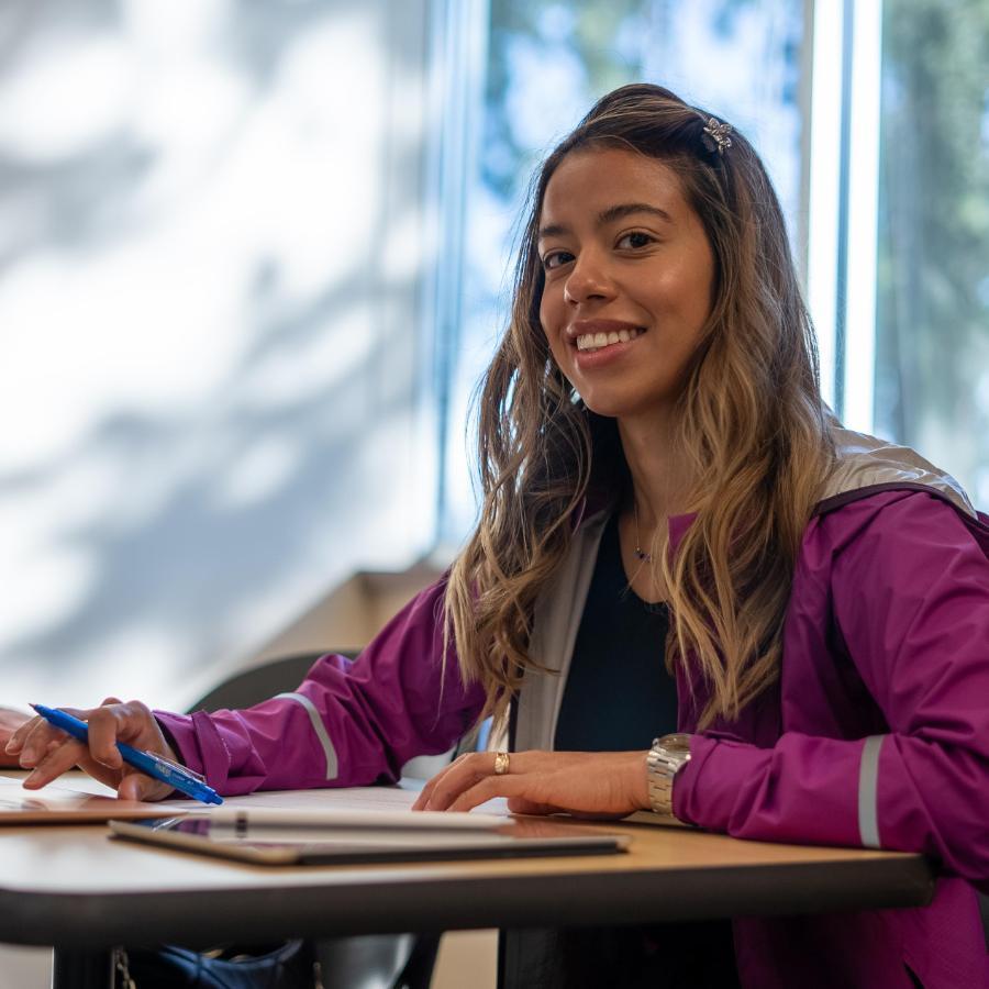 Female student smiling at table working on computer