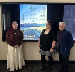 From left, North Idaho College student Elspeth Gibson, NIC Assistant Professor Lydia Ramus and NIC Associate Professor Philippe Valle stand in front of Gibson’s winning “Sunset on the Byway” poster design for The Festival at Sandpoint. Gibson won a $1,000 scholarship. The design will be featured on festival lineup posters, advertisements, the festival’s website, on a Toyota truck wrap and other ma