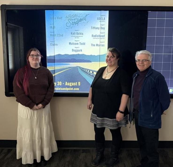 From left, North Idaho College student Elspeth Gibson, NIC Assistant Professor Lydia Ramus and NIC Associate Professor Philippe Valle stand in front of Gibson’s winning “Sunset on the Byway” poster design for The Festival at Sandpoint. Gibson won a $1,000 scholarship. The design will be featured on festival lineup posters, advertisements, the festival’s website, on a Toyota truck wrap and other ma