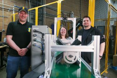 From left, Dan Blanchette, Jordan Reed and James Lasso stand behind Project S.P.L.I.N.T.E.R., an automated cedar plank inspection machine they designed and built as part of their engineering capstone project, in the U of I Coeur d’Alene lab.