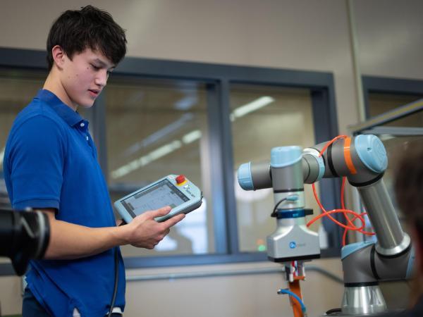 male CTE Student working a robotics with a command pad in hands