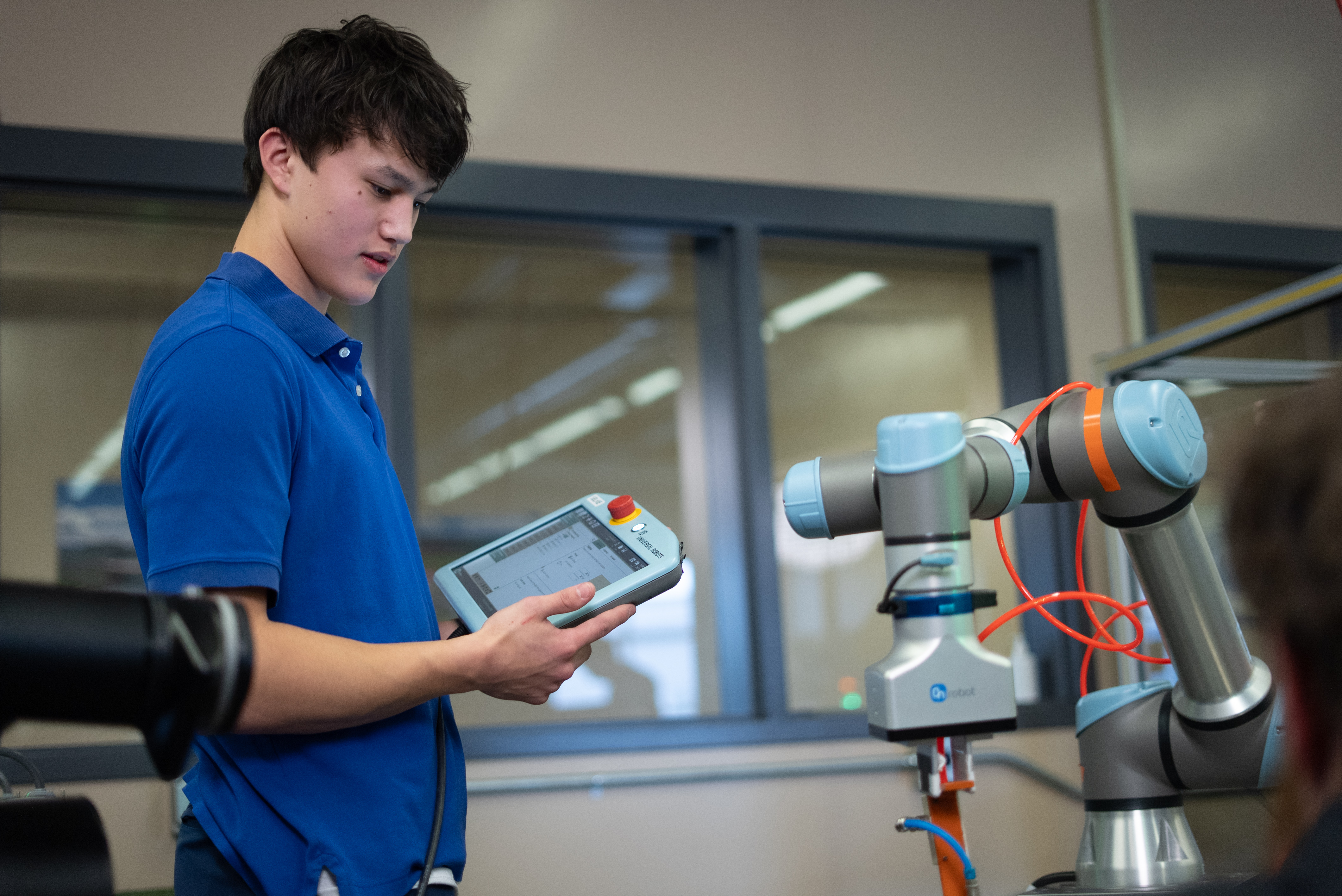 male CTE Student working a robotics with a command pad in hands