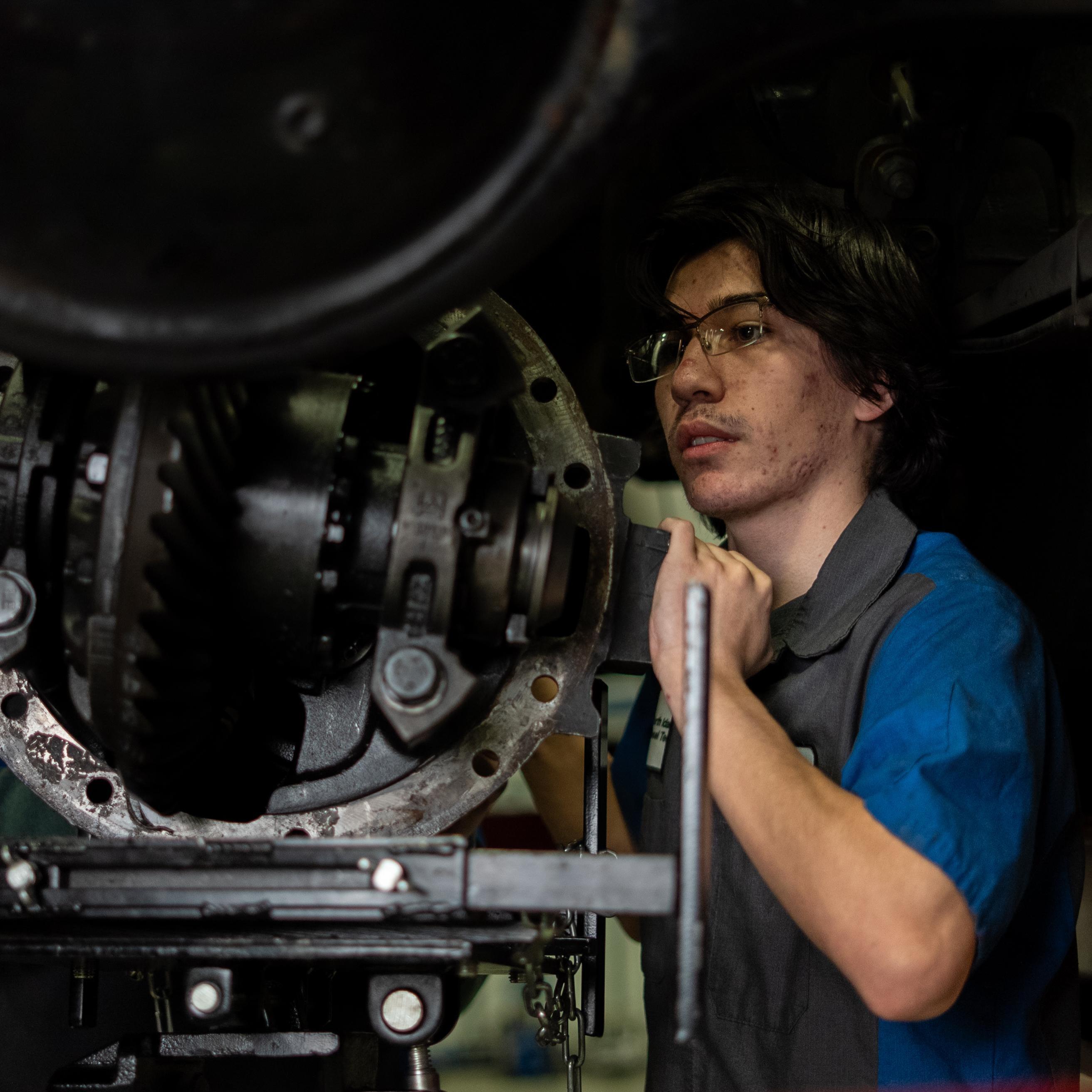  male Diesel Tech Student fixing hardware under lifted truck