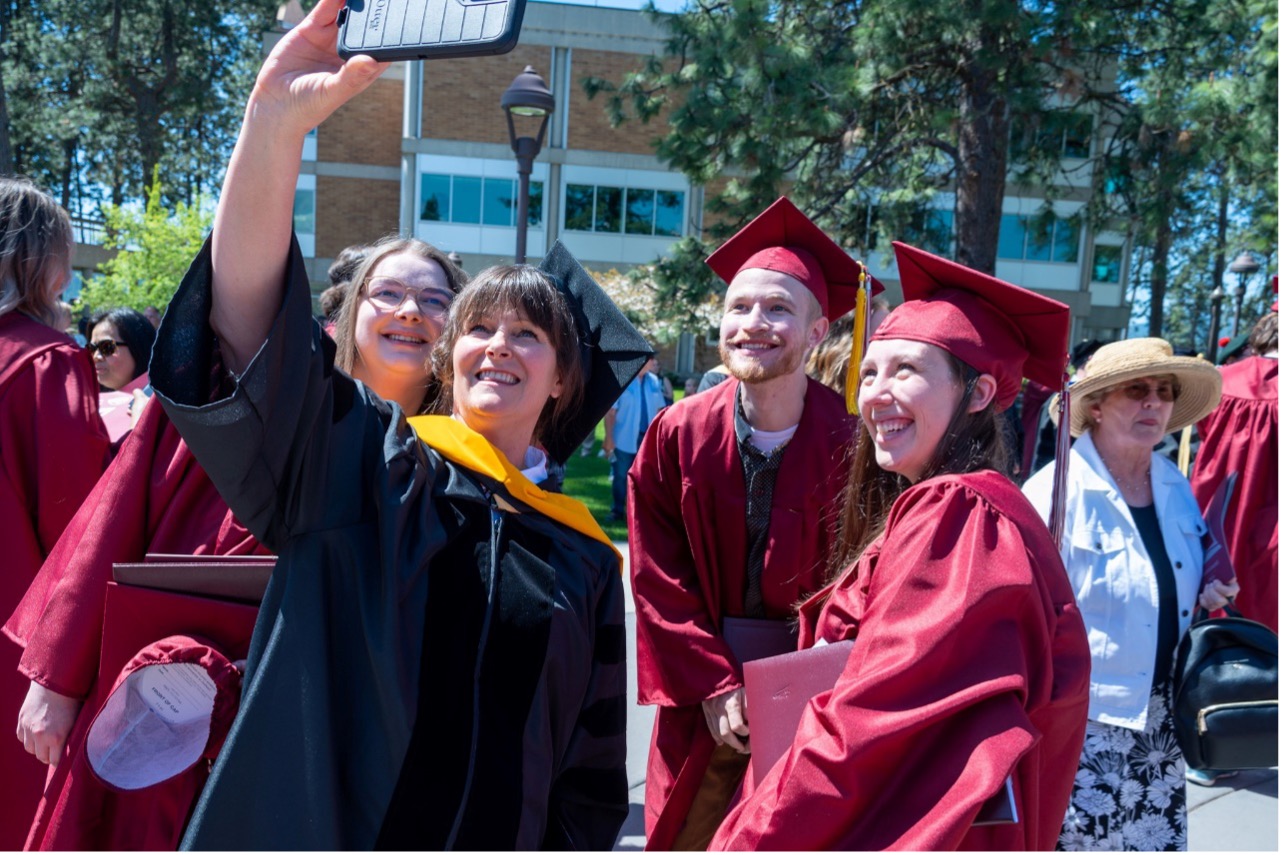 North Idaho College faculty member takes a celebratory selfie with 2024 student graduates.