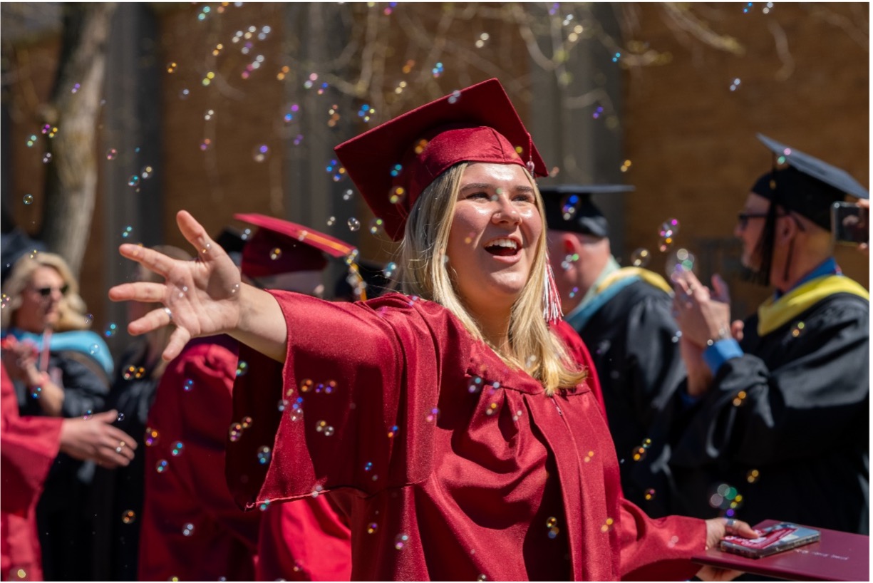 North Idaho College student joyously pops bubbles floating in the air during the 2024 Commencement Ceremony reception.